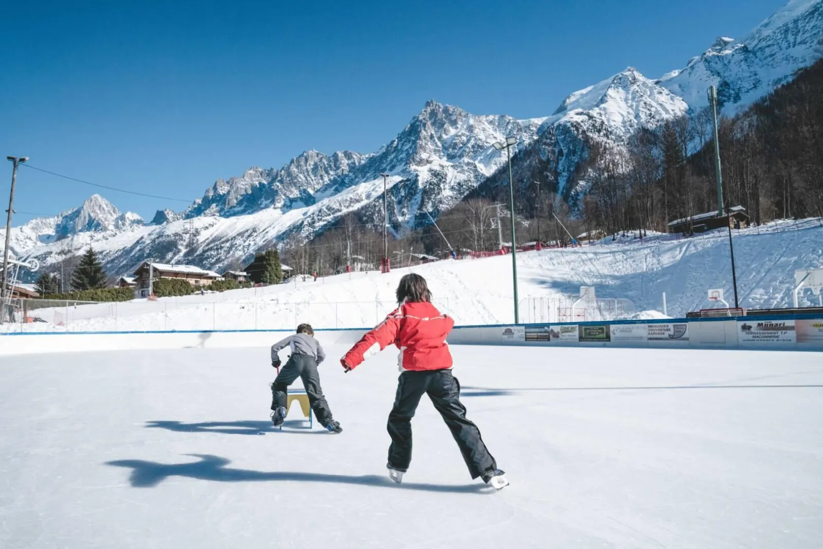 Two skaters on the Les Houches ice with the snowy Mont-Blanc range behind. — Patinoire des Houches