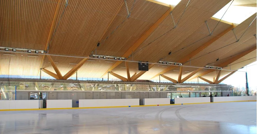 La glace vide de la patinoire de Samoëns sous sa toiture en bois, avec les bandes et les gradins le long du côté opposé. — Patinoire municipale de Samoëns