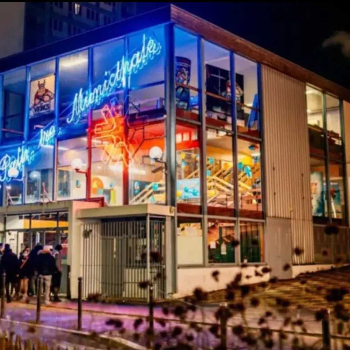 The glass-fronted building of the Patinoire municipale at night, with its blue neon sign and a few visitors queuing at the entrance. — Patinoire municipale de Vitry-sur-Seine