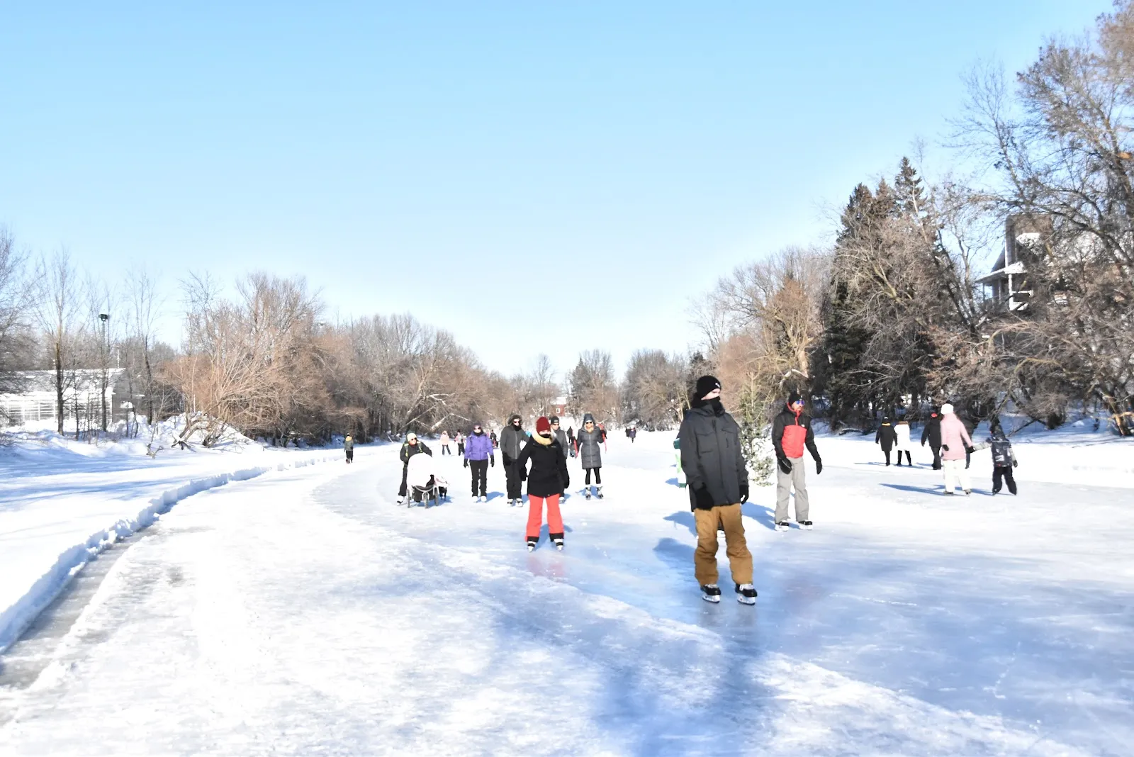 Skaters strung out along the groomed ice trail on the frozen L'Assomption river in Joliette on a clear winter day — Patinoire naturelle de la rivière L'Assomption