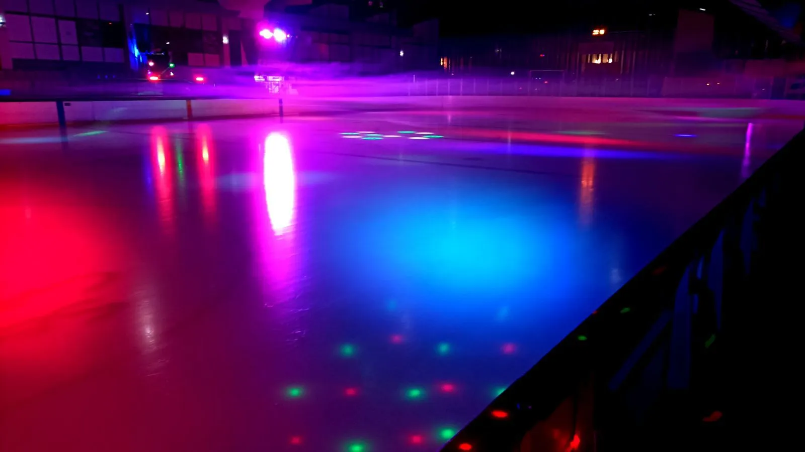The rink's ice lit in blue, pink and red by the evening light show, with no skaters on it — Patinoire olympique d'Amnéville