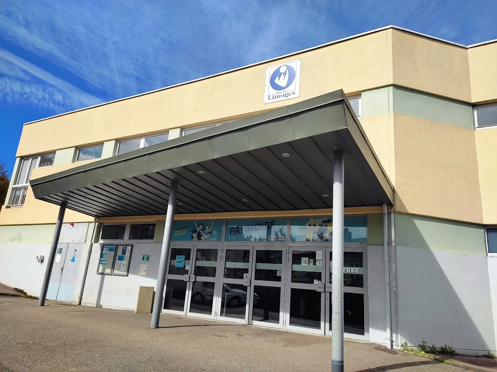 L’entrée de la patinoire de Limoges sous son auvent, avec le logo de la ville sur la façade de couleur crème — Patinoire Olympique de Limoges