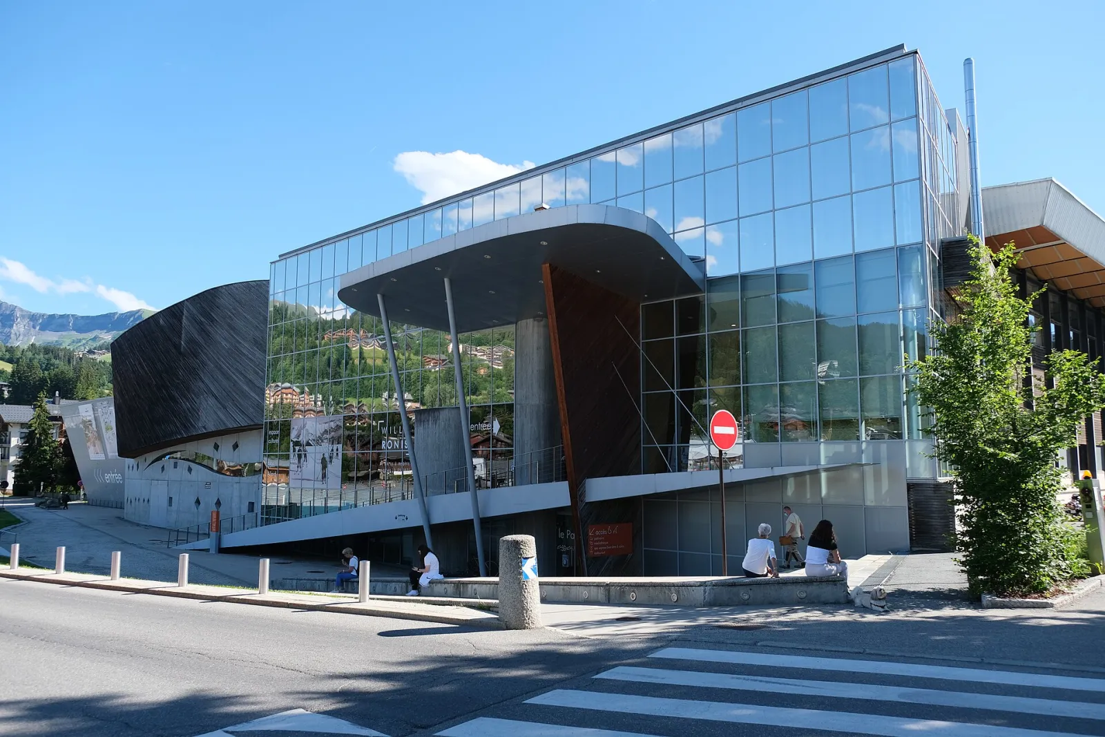 Glass and wood front of Le Palais, the Megève sports complex that houses the olympic ice rink, seen from the road. — Patinoire olympique (Le Palais Megève)