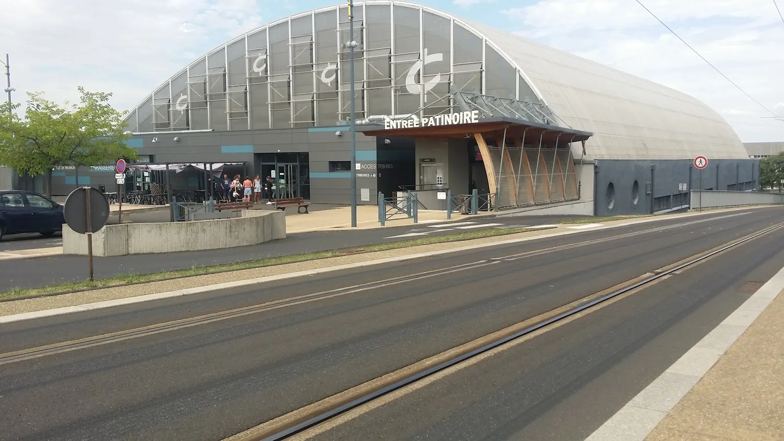 The barrel-vaulted patinoire seen from across the tram line, with the Entrée Patinoire sign over the entrance. — Patinoire Papadakis & Cizeron