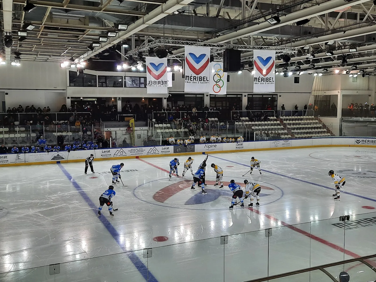Un match de hockey sur glace sur la patinoire du Méribel Ice Palace, avec les tribunes et la banderole des anneaux olympiques en arrière-plan — Patinoire du Parc Olympique de Méribel
