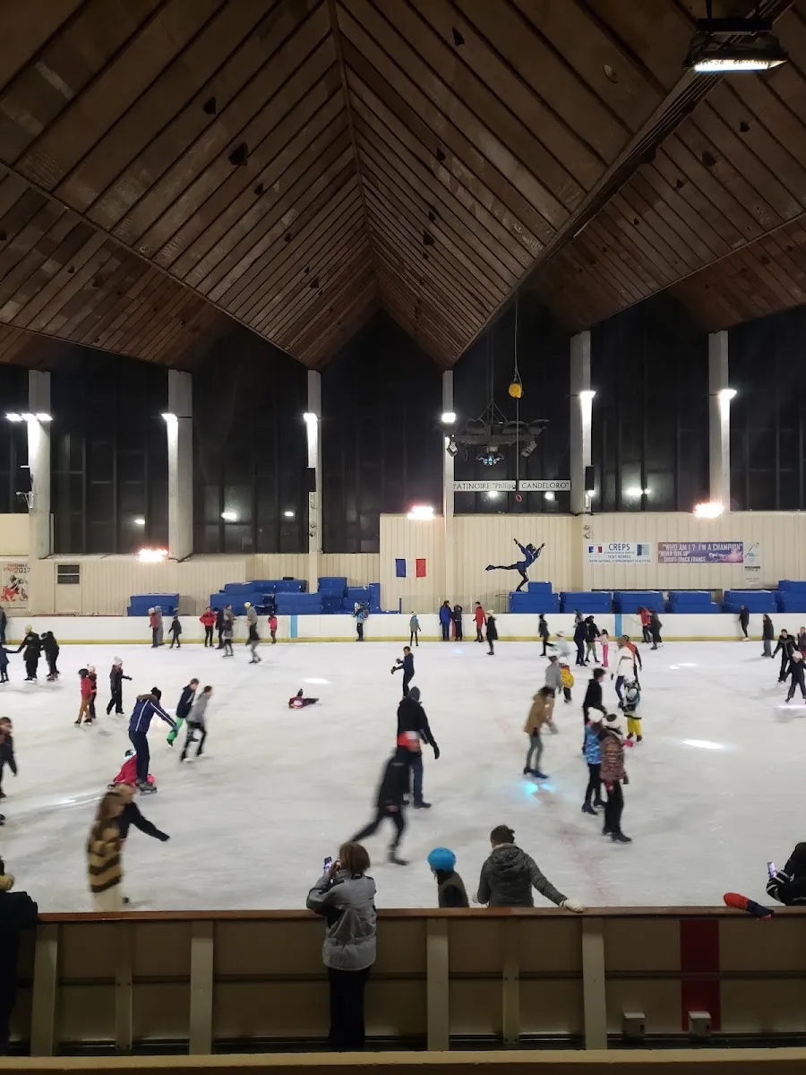The wide hall of the Font-Romeu rink under its pitched timber ceiling, with a public session in progress and the CREPS altitude-training banners on the end wall. — Patinoire Philippe Candeloro