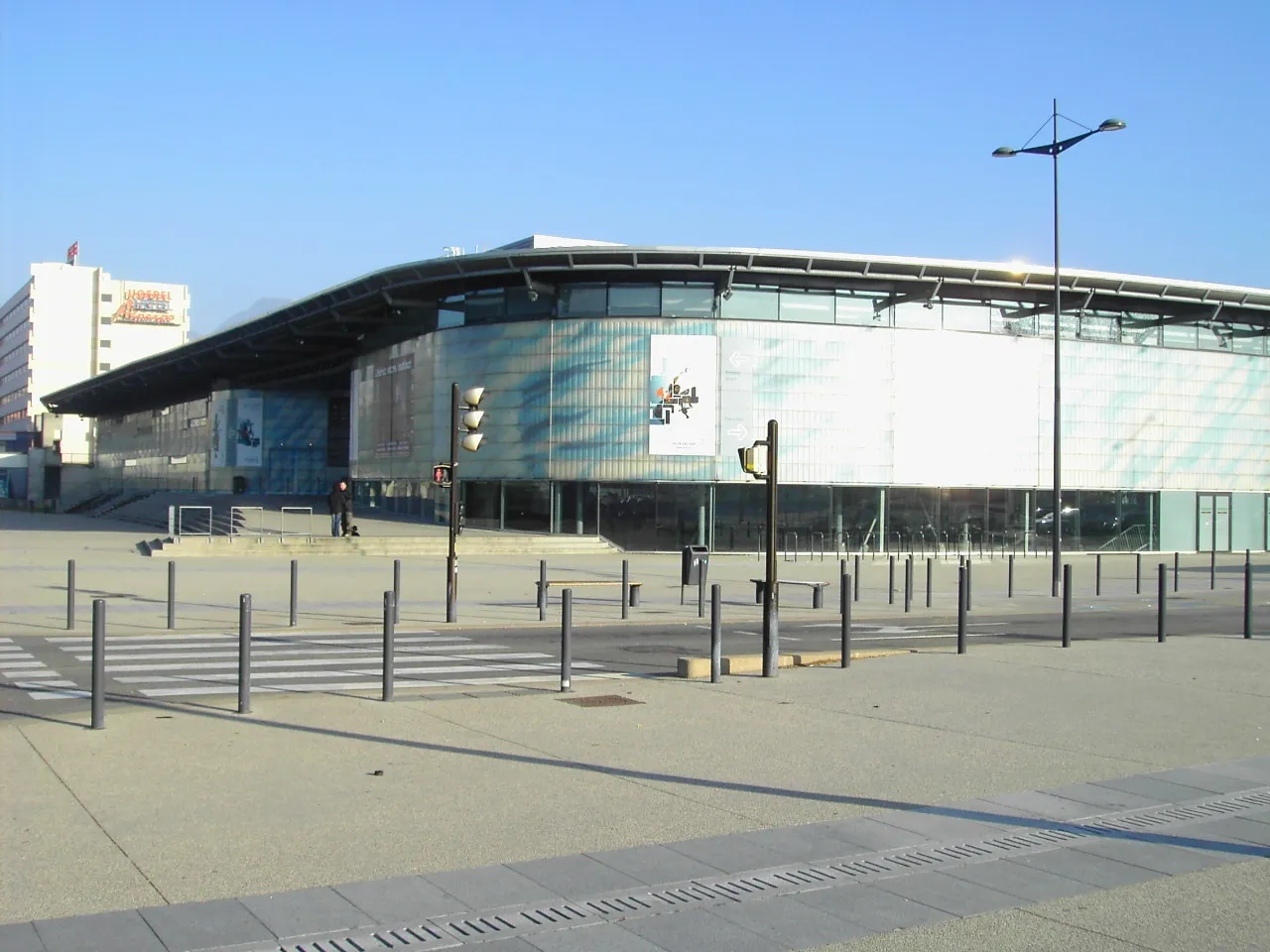 The curved glass-and-metal roof line of the Polesud building seen across the forecourt on a clear day — Patinoire Polesud