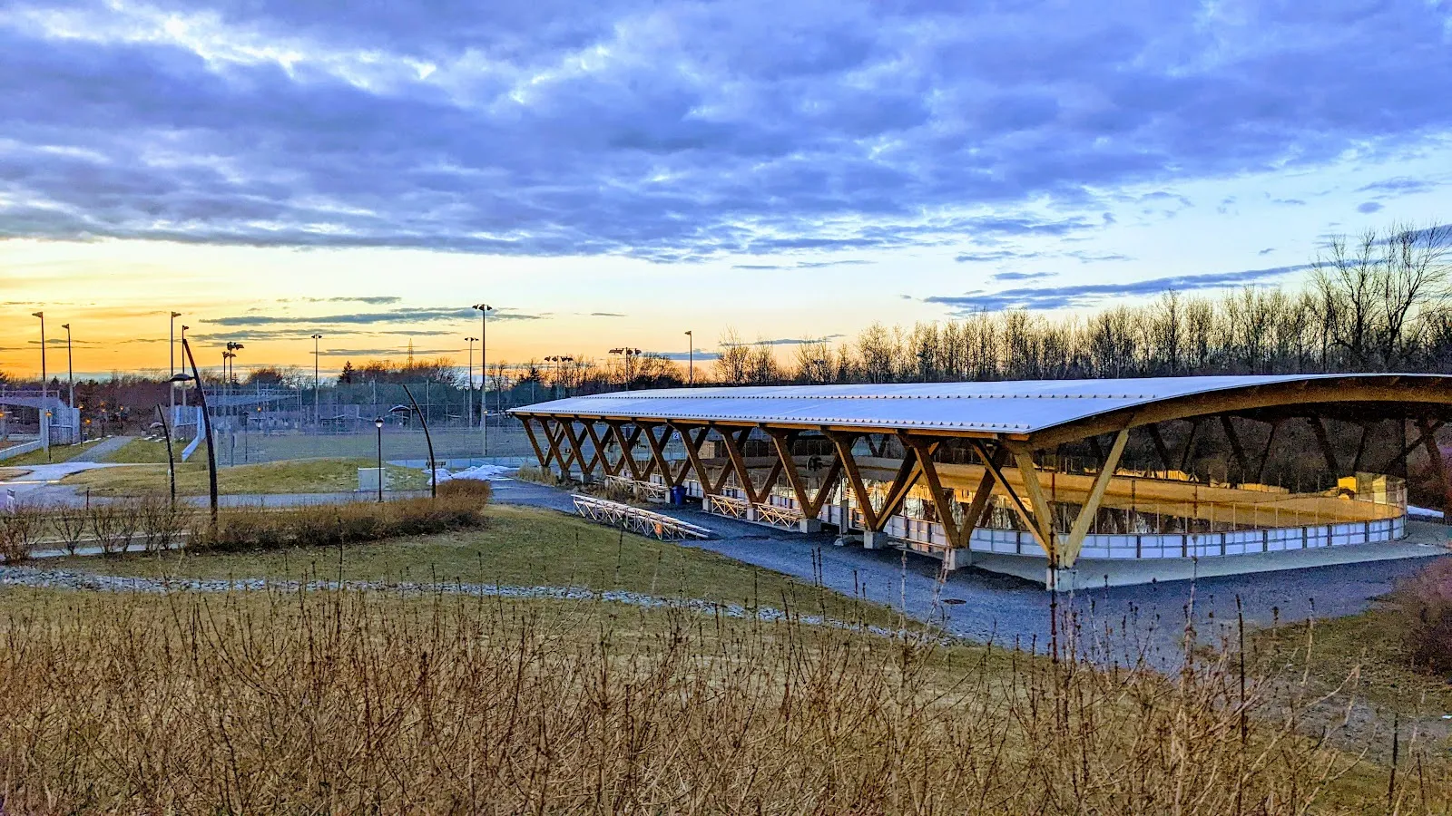 The covered refrigerated rink at Parc Haendel in Candiac at dusk, under its timber roof — Patinoire réfrigérée couverte du parc Haendel