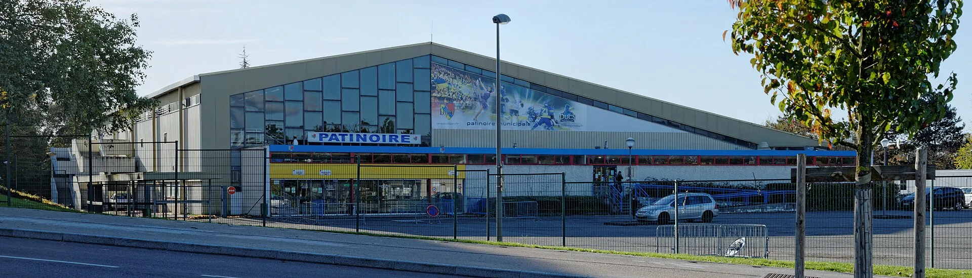 The front of the Patinoire Trimolet seen from the boulevard, with its PATINOIRE sign over the glazed entrance and the hall's long low roof. — Patinoire Trimolet