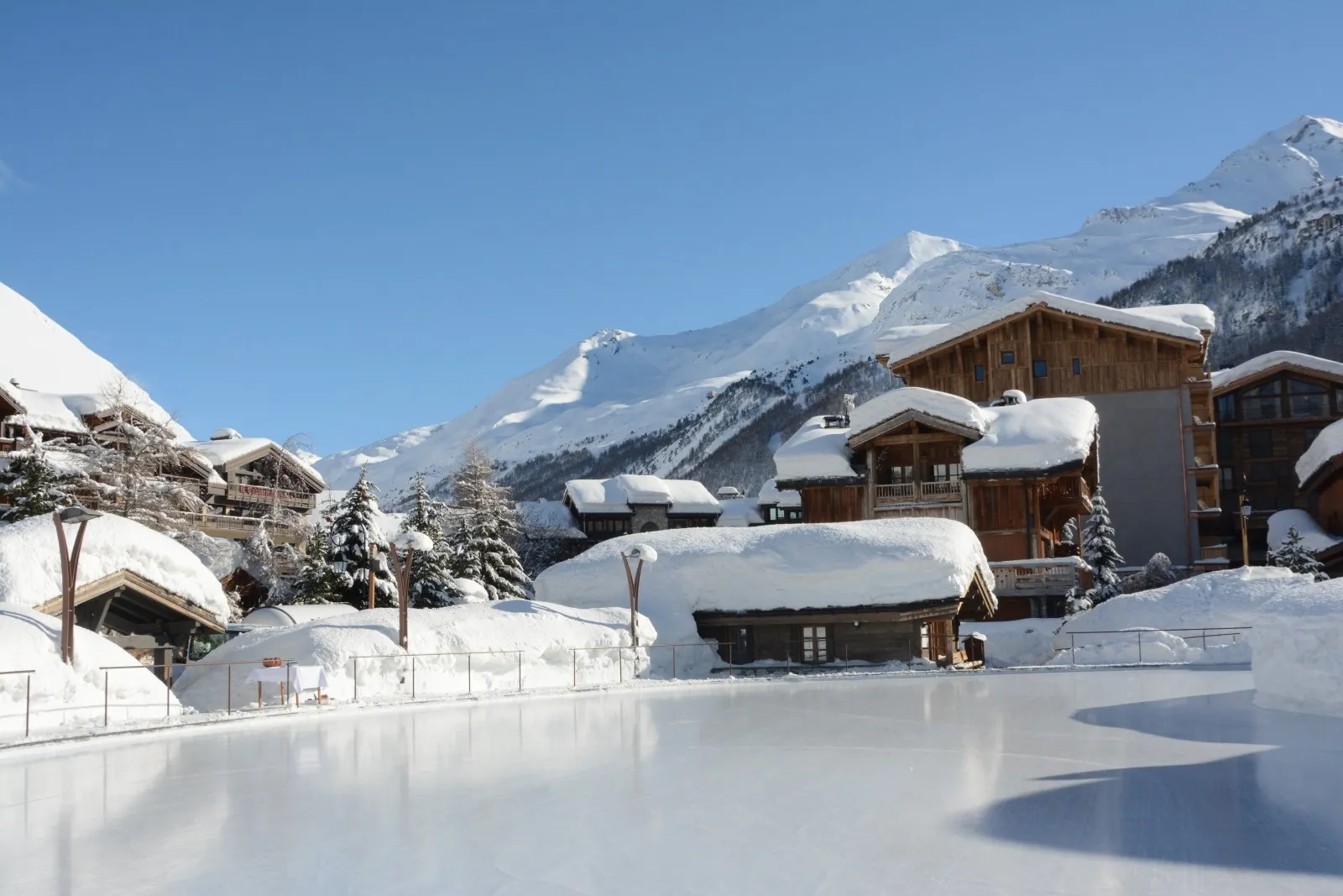 The open-air rink in Val d'Isère from the edge of the ice, with snow-laden chalets and the mountain behind. — Patinoire de Val d'Isère