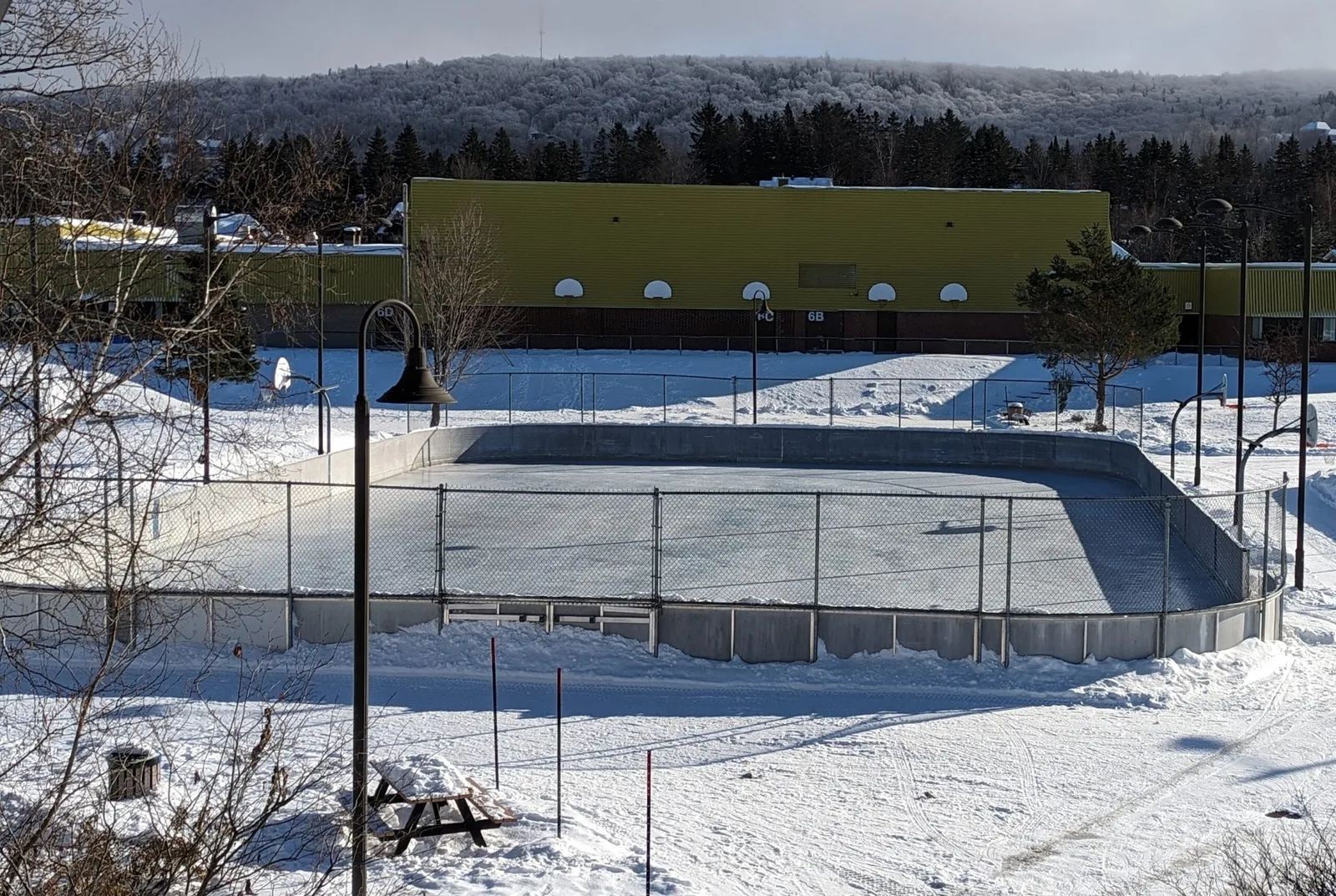 The small outdoor rink at Parc Carrier-Chamberland in Lac-Beauport in winter, with its boards and the park building behind. — Patinoires du parc Carrier-Chamberland