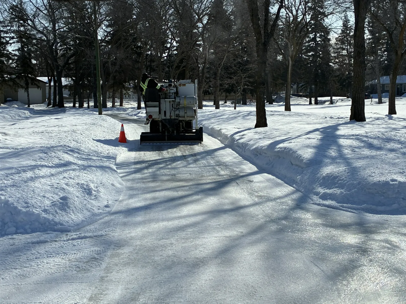 The skating pathway through the trees of the park, with a resurfacing machine at work on the ice and snowbanks along both sides. — Patrick Park Skating Pathway (Yorkton)
