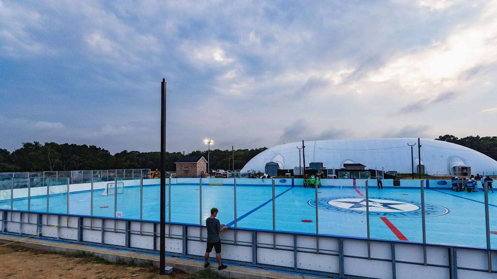 The Peconic Ice Rinks white air dome at dusk, with the open-air dek rink and its star logo in the foreground — Peconic Ice Rinks