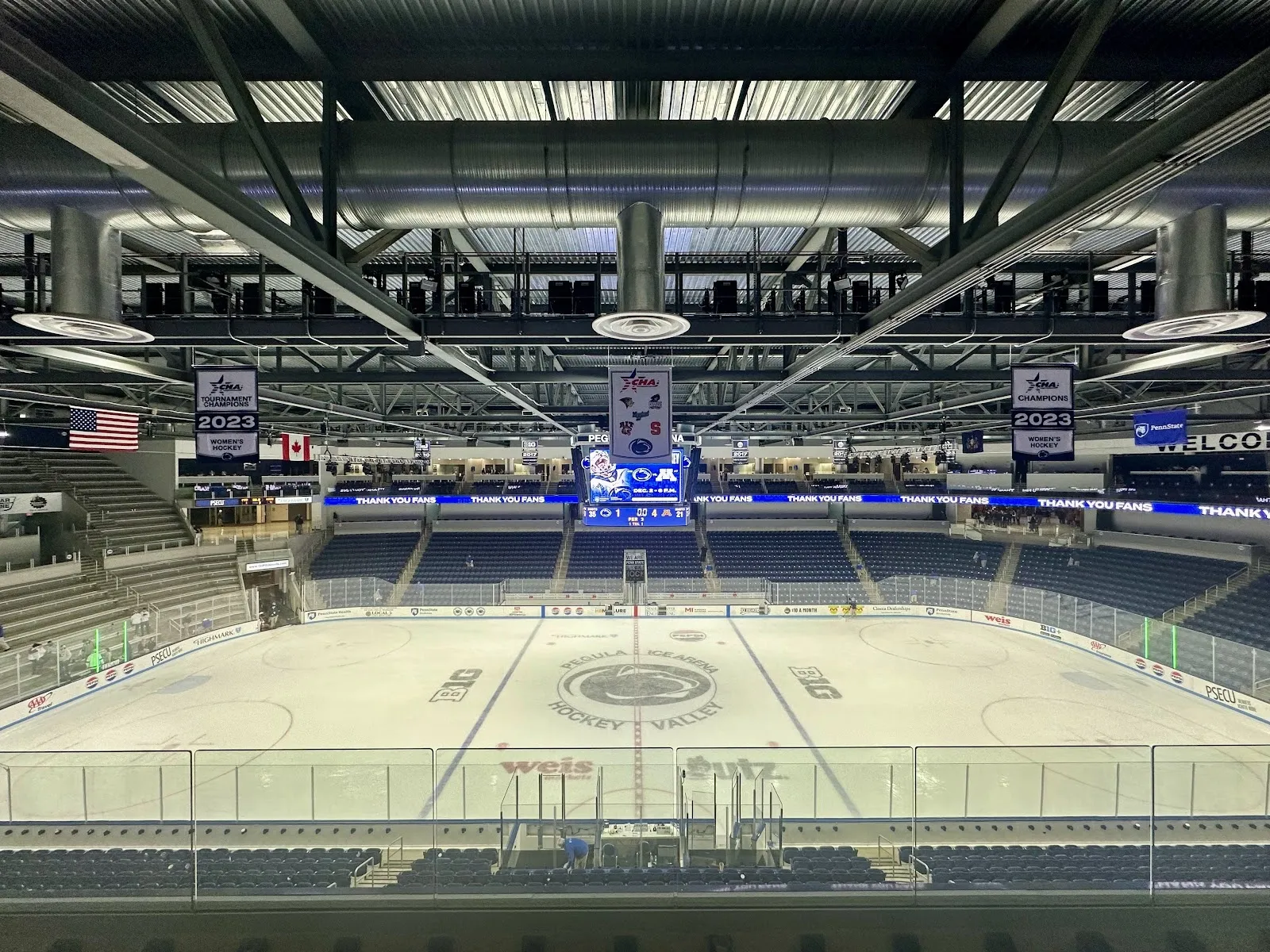 La arena vista desde un asiento alto, con la pista vacía y el logotipo central de Hockey Valley, rodeada de asientos azul oscuro bajo un techo de armaduras. — Pegula Ice Arena (Penn State)
