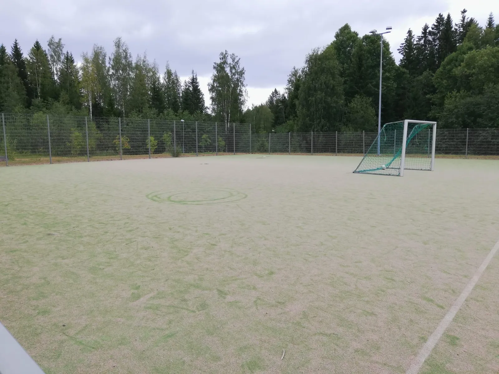 The fenced pitch at Peikkometsä in Kuopio, which serves as a skating field in winter, seen in summer with a goal and floodlight masts along its edge. — Peikkometsän luistelukenttä