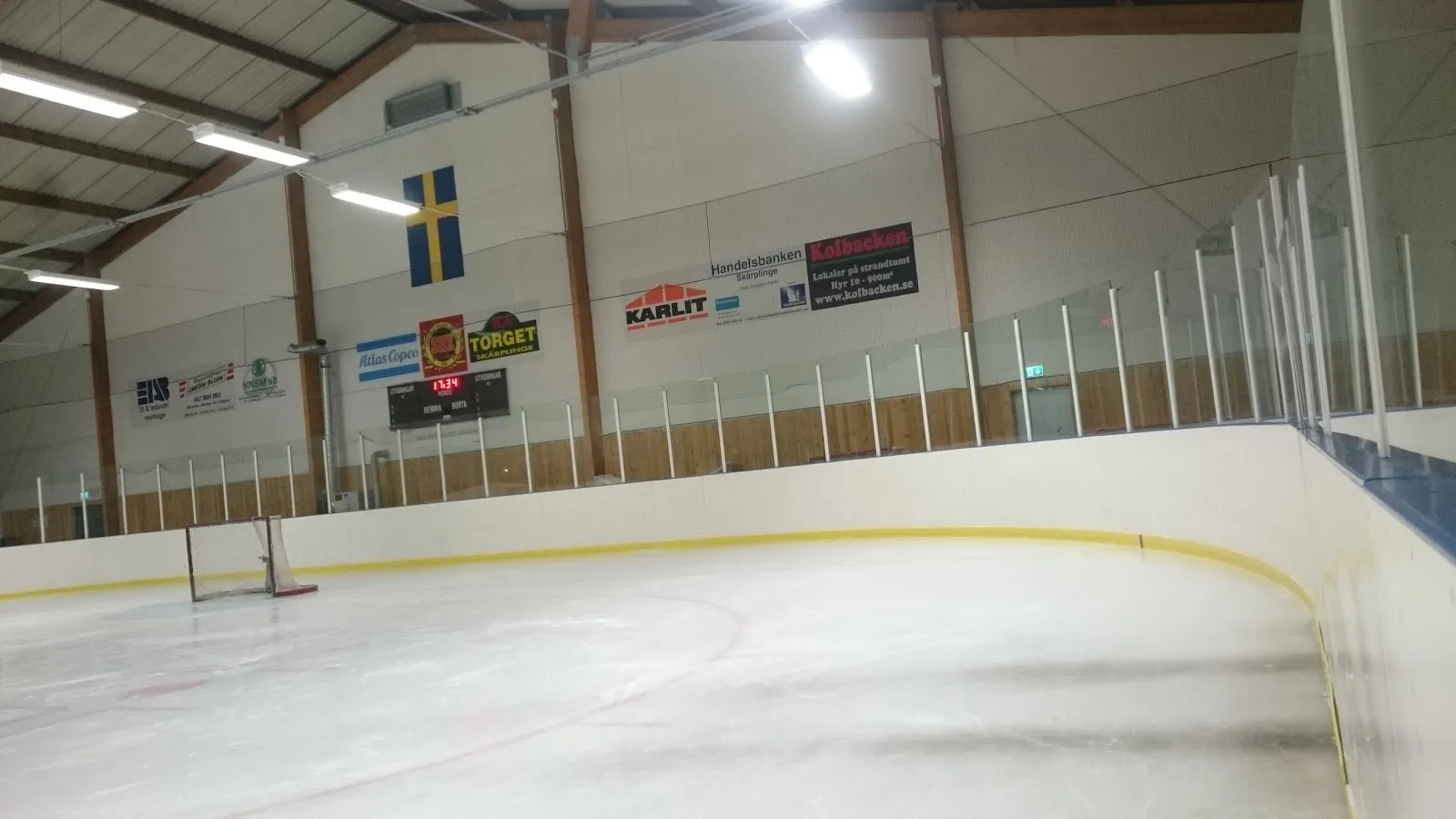 The empty ice sheet in PEK-hallen in Skärplinge with the Swedish flag, scoreboard and sponsor boards at the far end — PEK-hallen