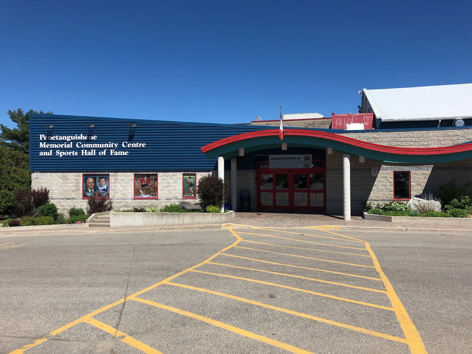 The blue-clad front of the Penetanguishene Memorial Community Centre and Sports Hall of Fame, with a curved red canopy over the doors. — Penetanguishene Memorial Community Centre