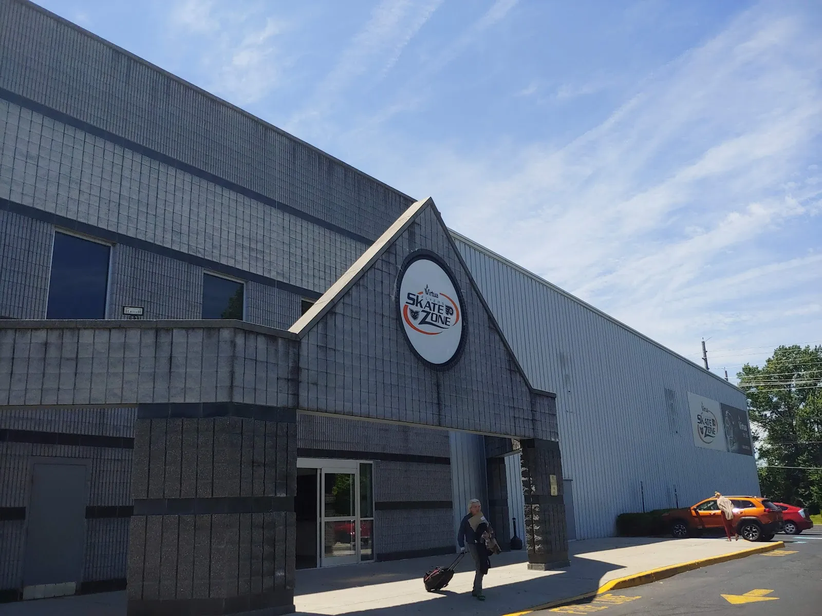 The grey block entrance gable with a round Skate Zone sign, and the long metal-sided rink hall running back from it. — Pennsauken Skate Zone