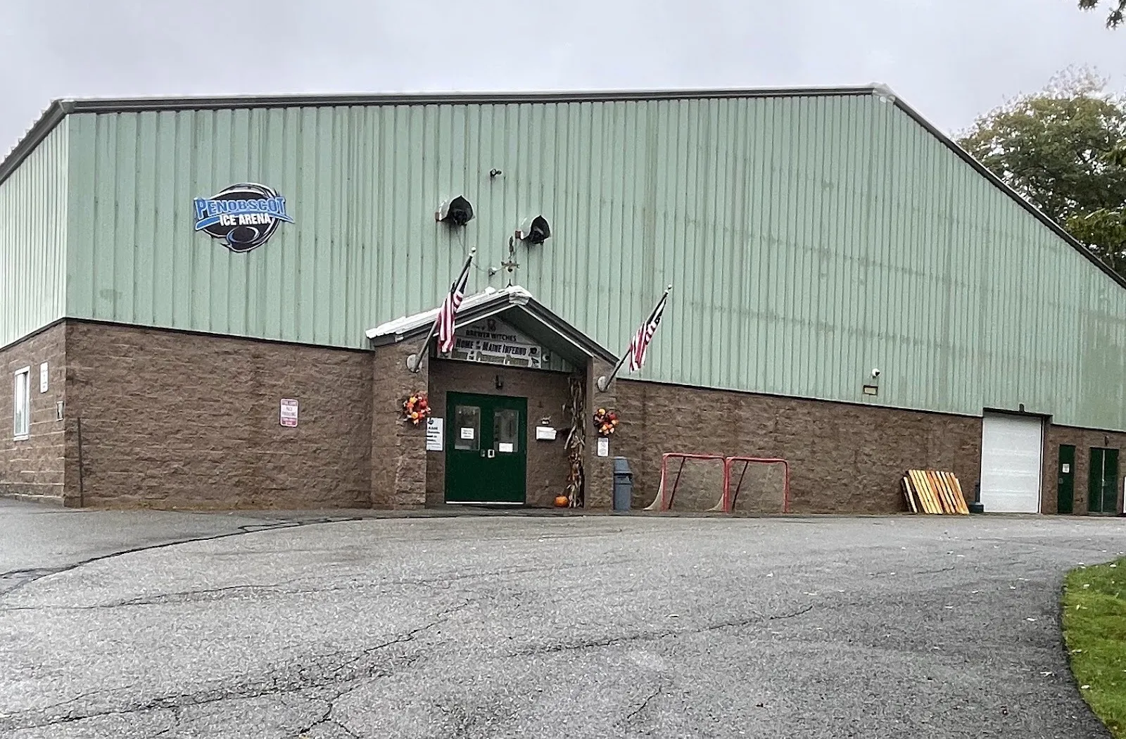 The Penobscot Ice Arena building, its logo on the pale green metal hall above a brick base and a flag-flanked green door — Penobscot Ice Arena