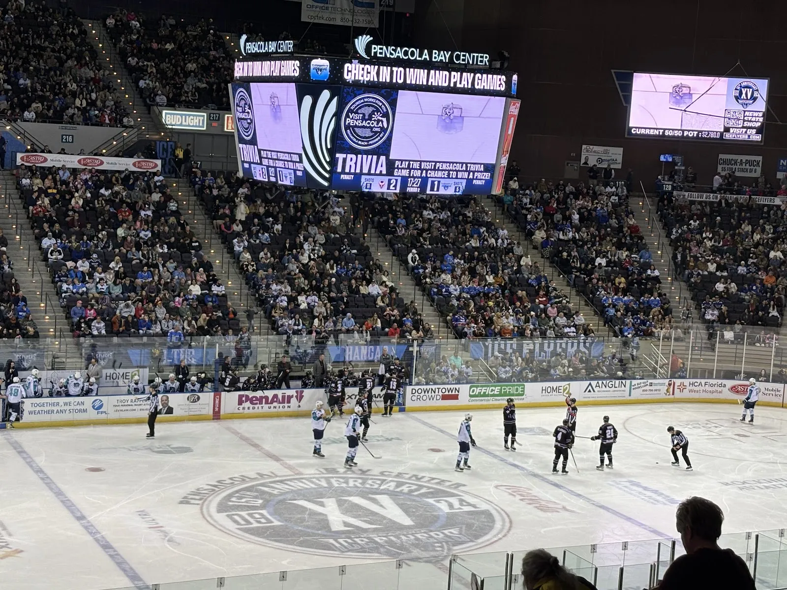 An ice hockey game at the Pensacola Bay Center, players spread across the ice with the arena seating bowl and scoreboard behind — Pensacola Bay Center