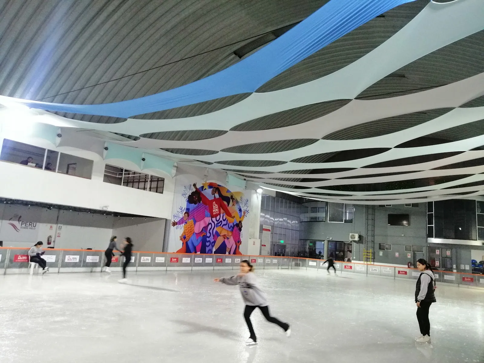 La pista de hielo bajo el techo abovedado del recinto en San Borja, con un mural en la pared del fondo y algunos patinadores — Peru On Ice