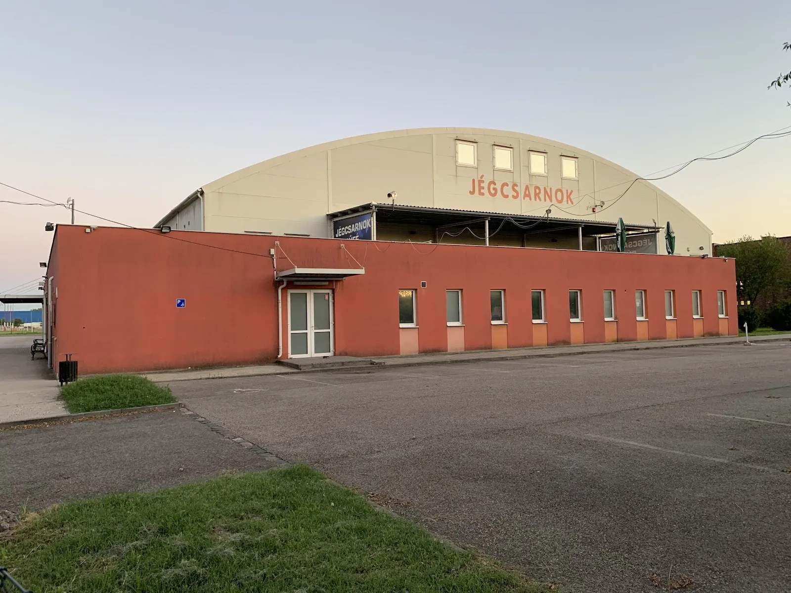 Az íves tetejű pesterzsébeti jégcsarnok és piros melléképülete a parkolóból nézve – ESMTK Pesterzsébet Jégcsarnok