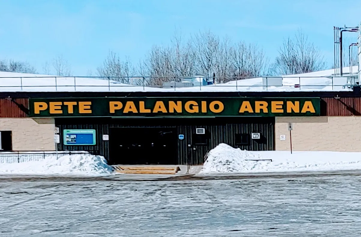 El frente de Pete Palangio Arena en North Bay, con el nombre de la arena en letras doradas grandes sobre la entrada y bancos de nieve al frente — Pete Palangio Arena