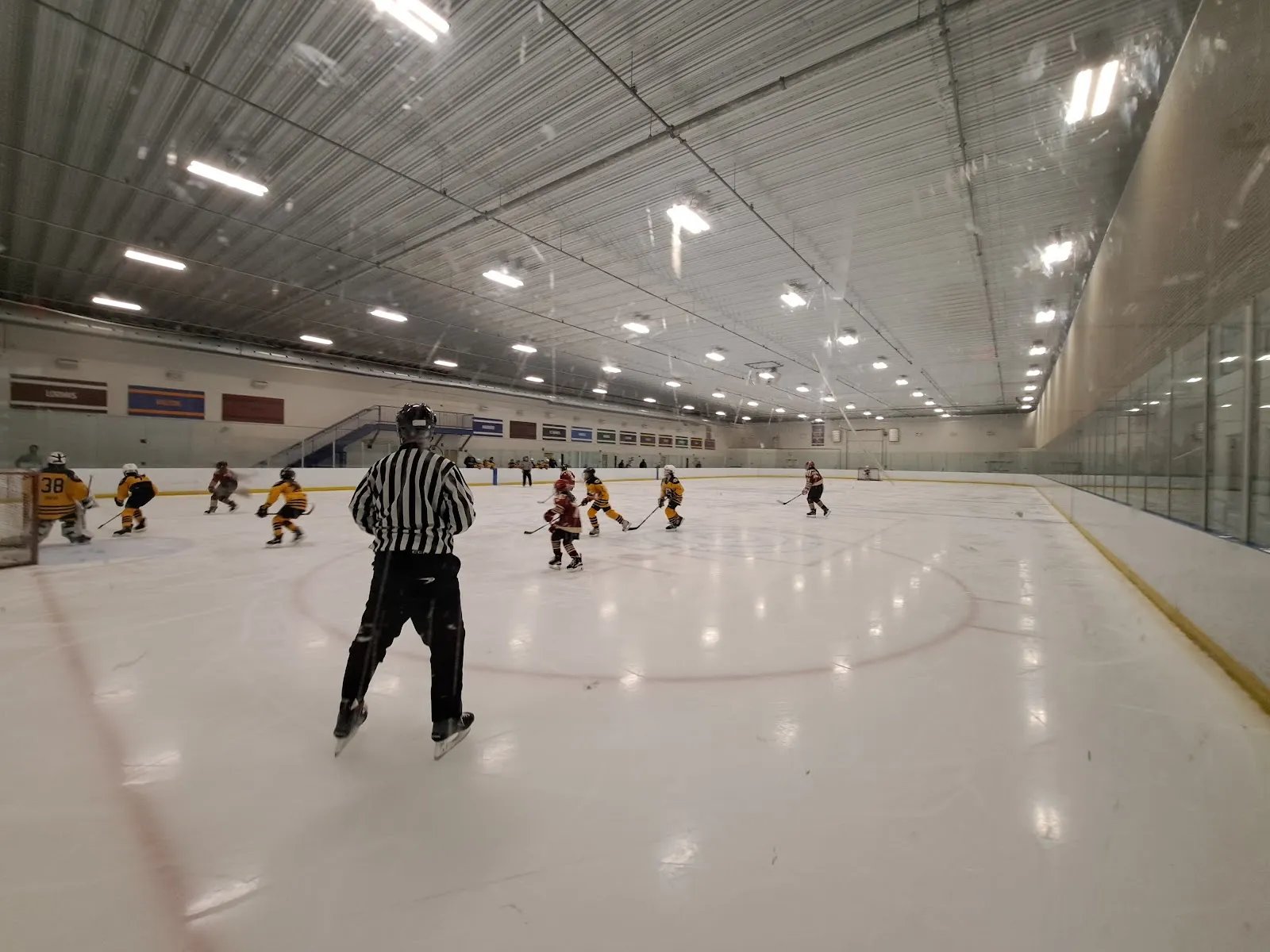A youth hockey game on the indoor ice at Phillips Academy with a referee and players at the far end — Phillips Academy Ice Rinks