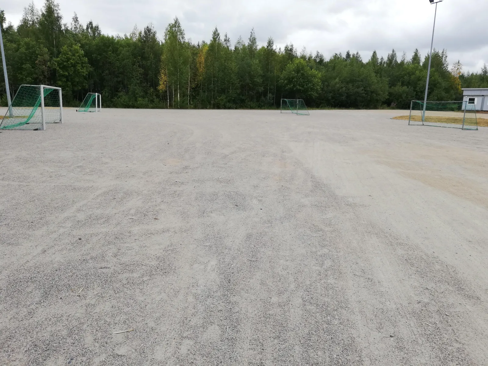 The gravel field at the Pirtti school in Kuopio, which serves as a skating field in winter, seen in summer with goals and woods behind. — Pirtin koulun luistelukenttä
