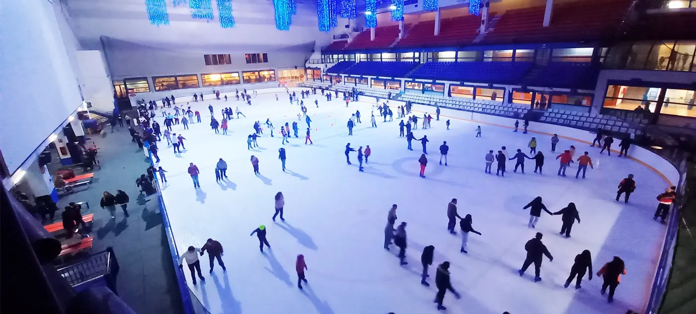A wide view of a public session at the Palacio de Hielo in Madrid, skaters spread across the whole sheet under the lit hall. — Pista de Hielo de Madrid