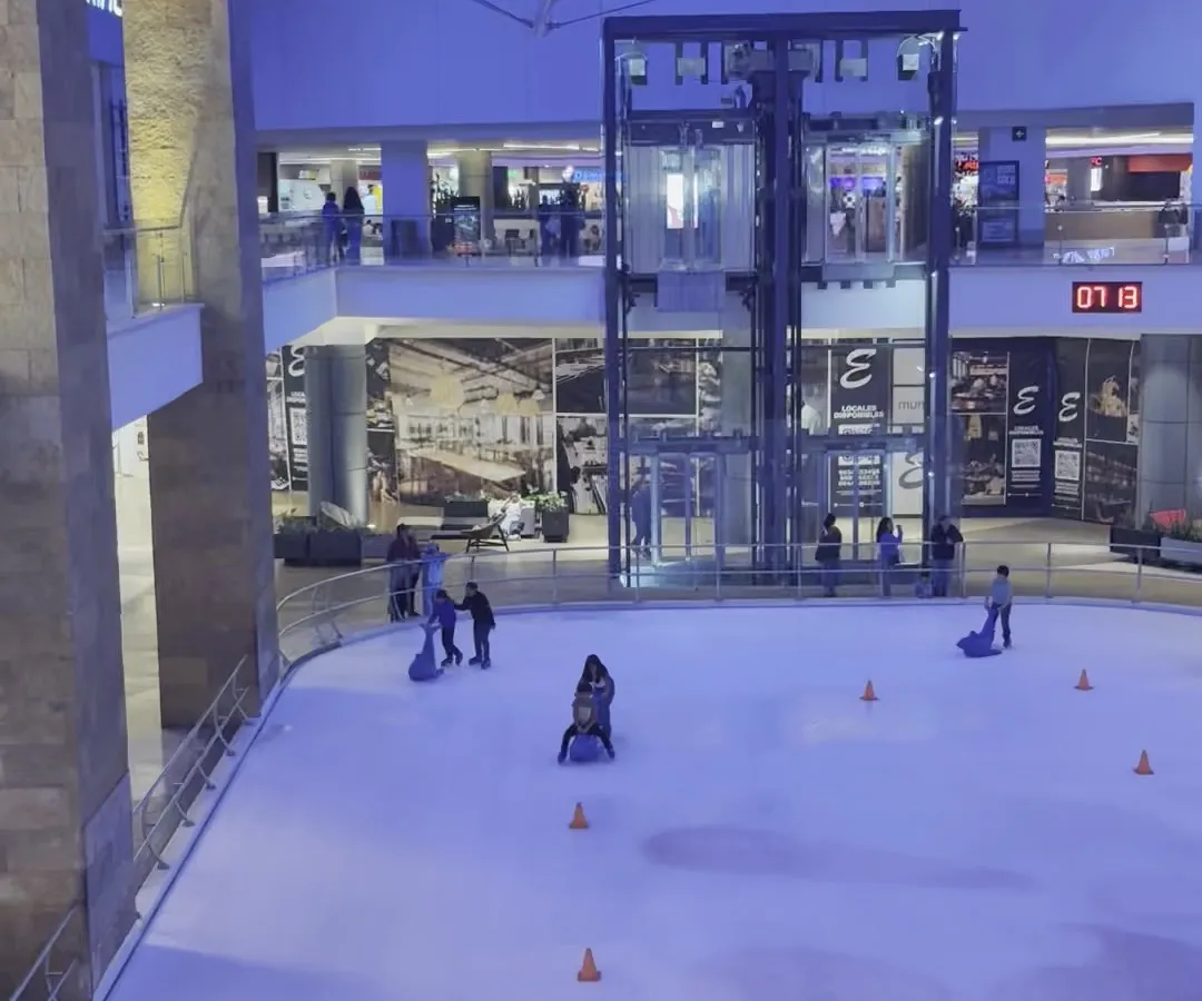 The Mundo E rink seen from the upper level, with the glass elevators and shops of the atrium behind it — Pista de Hielo ¡Recórcholis! Mundo E
