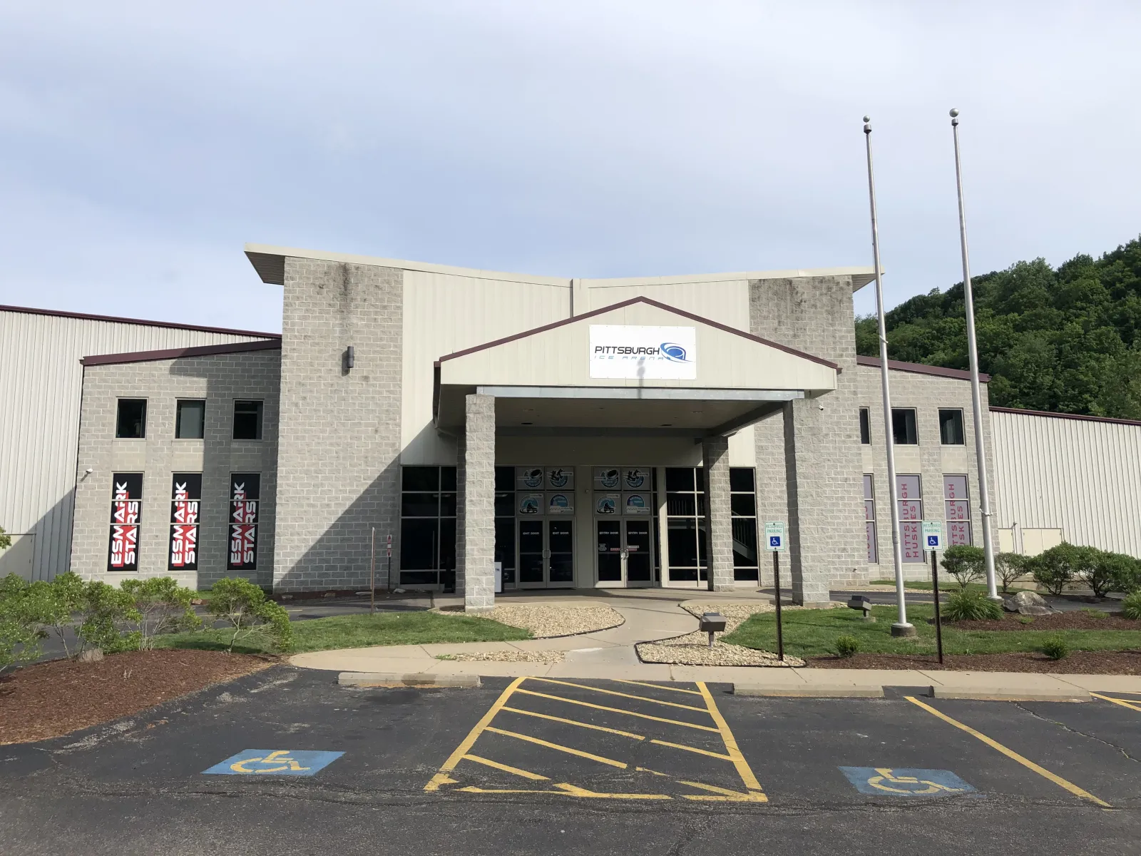 Front entrance of the building with a "Pittsburgh Ice Arena" sign over the doors, flagpoles and parking lot in front — Pittsburgh Ice Arena