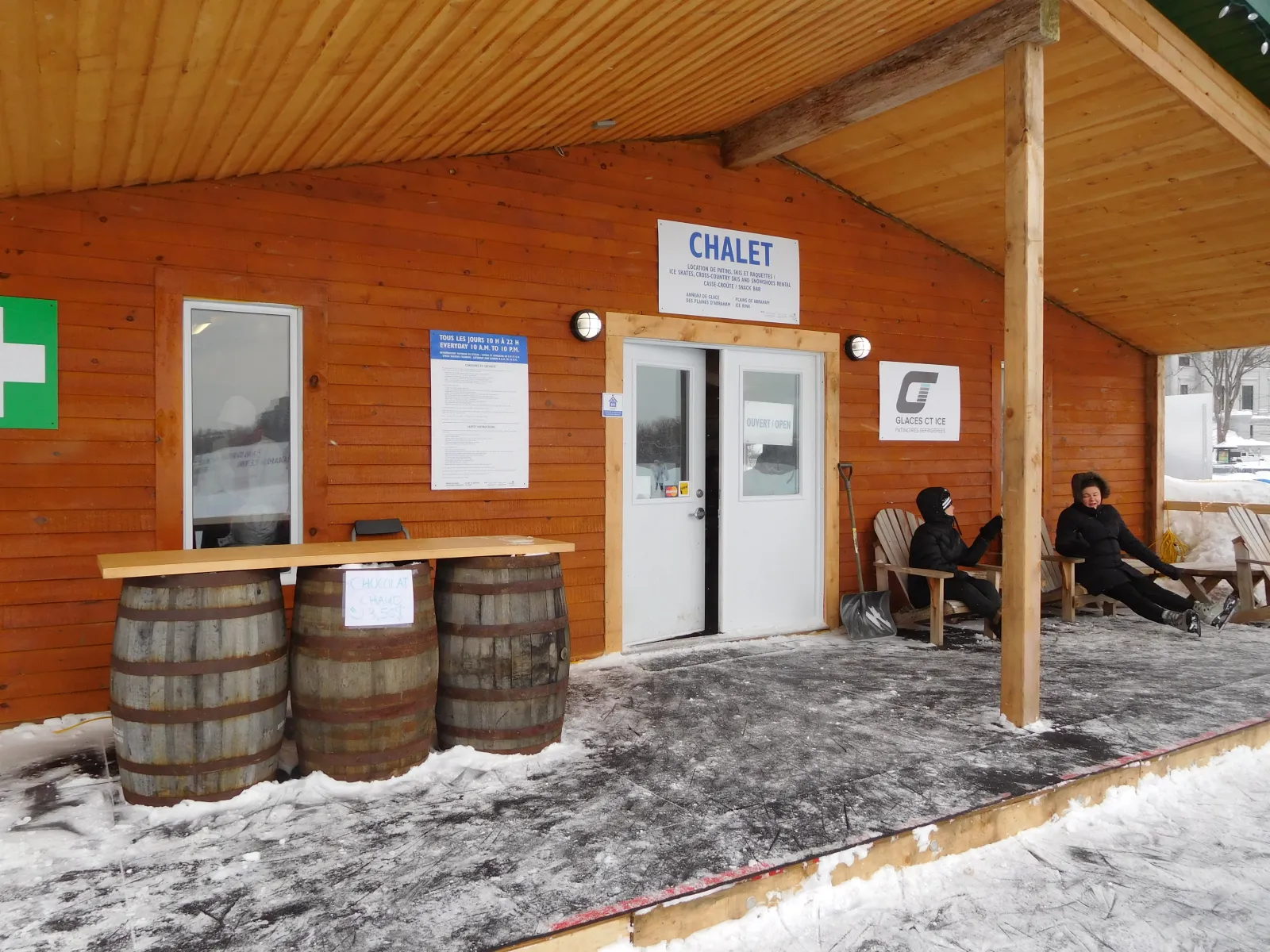 The wooden skaters' chalet beside the Plains of Abraham skating oval, with barrels and benches under its covered porch — Plains of Abraham Skating Oval (Anneau de glace des plaines d'Abraham)