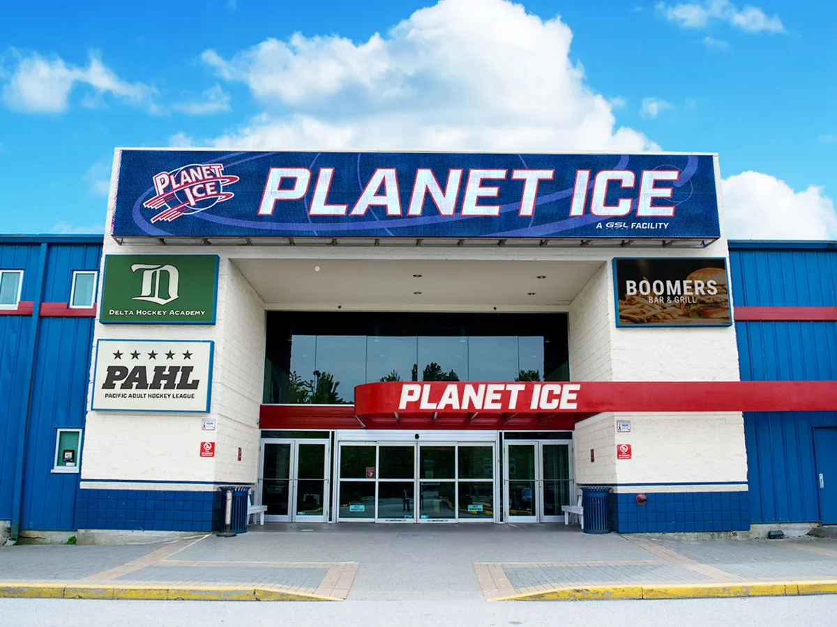 The white entrance block with a PLANET ICE banner, Delta Hockey Academy, PAHL and Boomers signs, set in the blue-clad arena building. — Planet Ice Delta