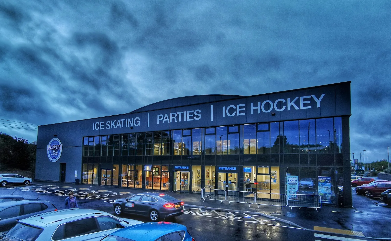 The glass-fronted two-storey front of the arena at dusk, with 'Ice Skating | Parties | Ice Hockey' lettering above the entrances. — Planet Ice Leeds