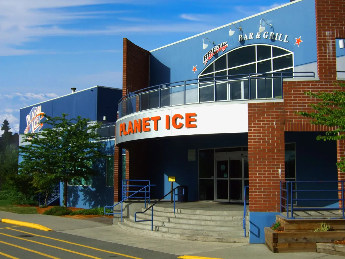 The red-brick entrance with a curved PLANET ICE sign, front steps, and the Bar & Grill balcony above. — Planet Ice Maple Ridge