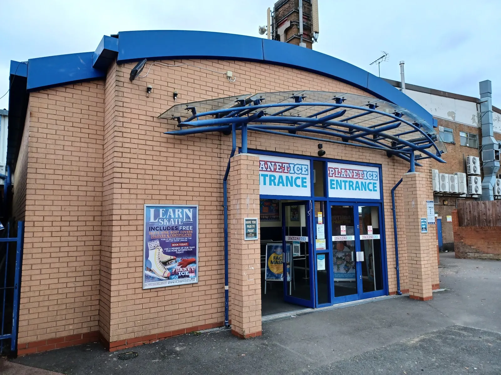 The brick entrance block with a curved blue canopy and two 'Planet Ice ENTRANCE' signs above the glass doors. — Planet Ice Solihull