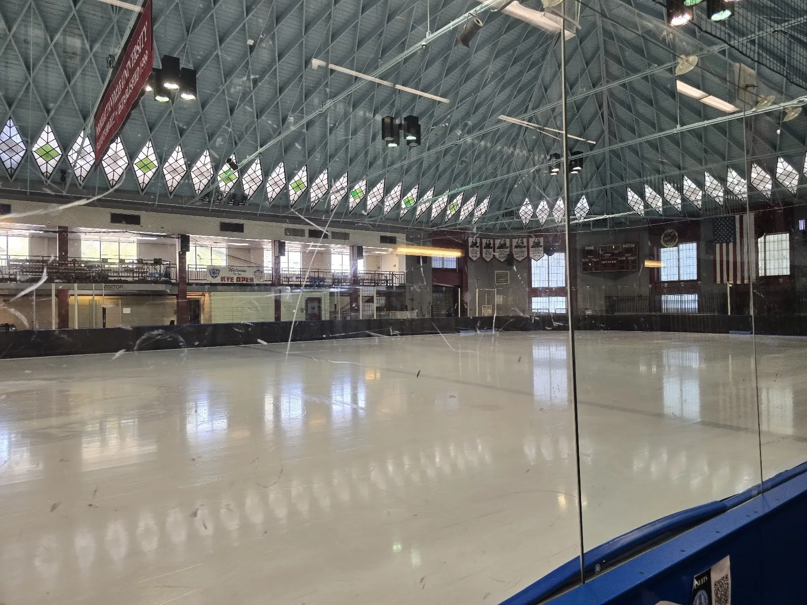 El hielo vacío bajo el techo de enrejado de vidrio del antiguo edificio de Playland, con un barandal de franja azul curvándose en primer plano. — Playland Ice
