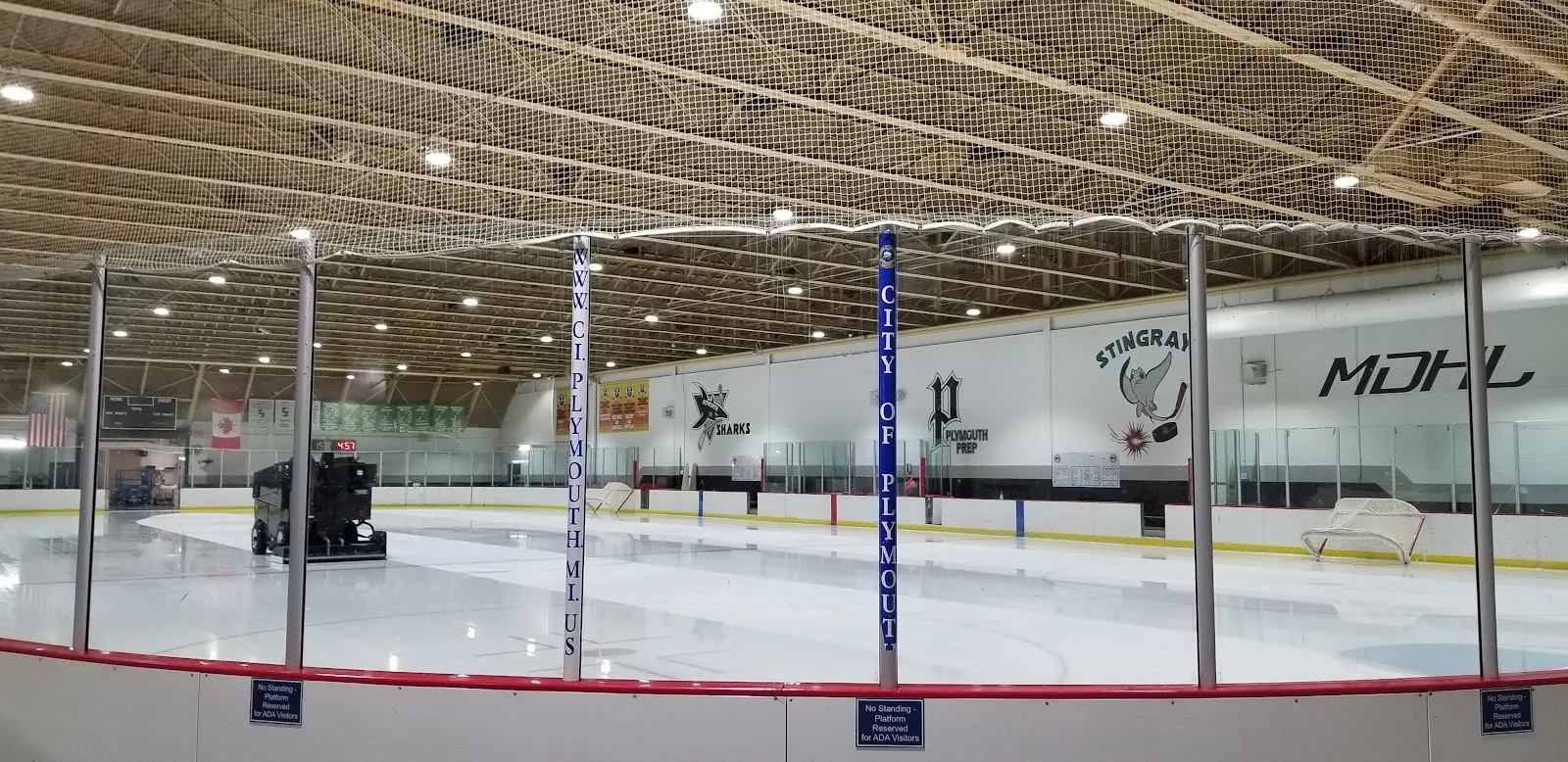 The empty sheet along the glass under a timber-beamed ceiling, white boards lettered with the league name curving round the end of the rink. — Plymouth Cultural Center Ice Arena