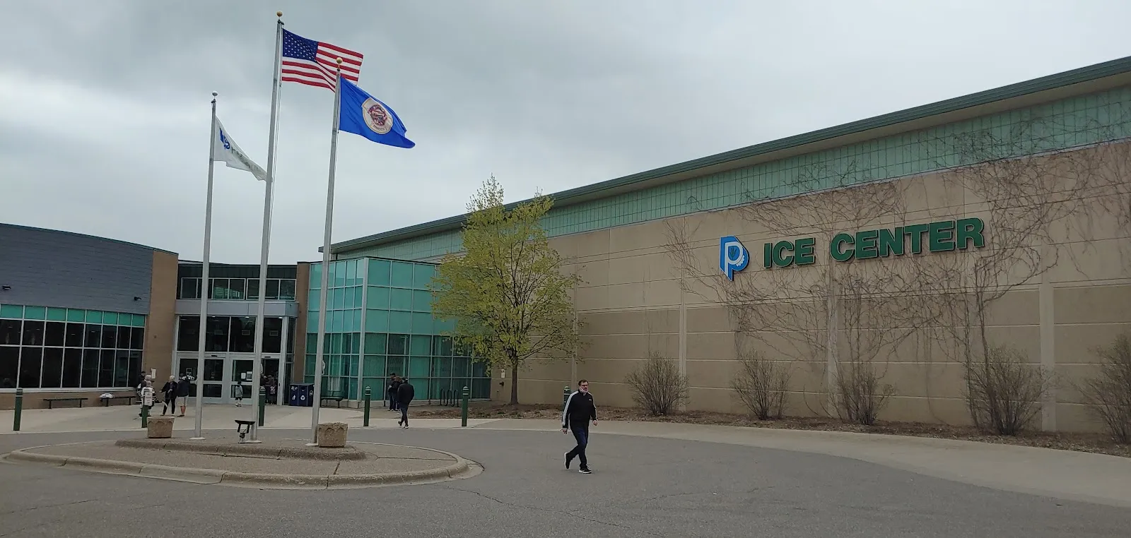 The Plymouth Ice Center entrance with flags flying beside the glass-fronted building and parking. — Plymouth Ice Center