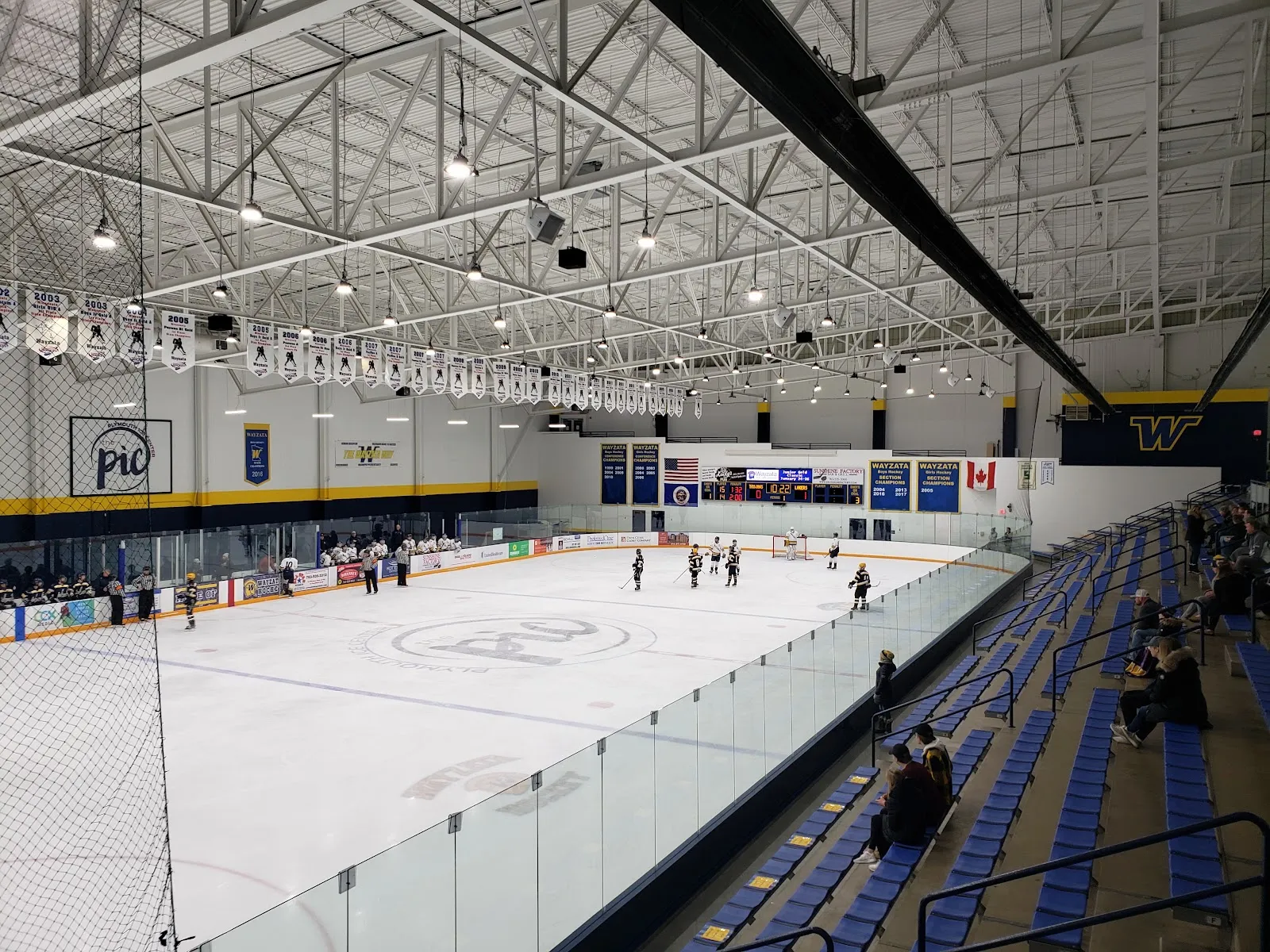 A wide view along the Plymouth Ice Center rink with its boards, bleachers and a few skaters in the distance. — Plymouth Ice Center