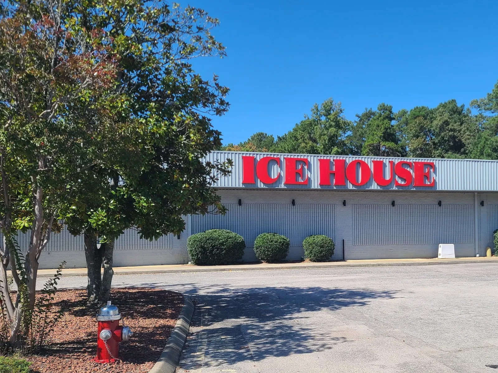 The long grey metal building with red ICE HOUSE lettering along its front, seen from the parking lot on a sunny day. — Polar Ice Cary