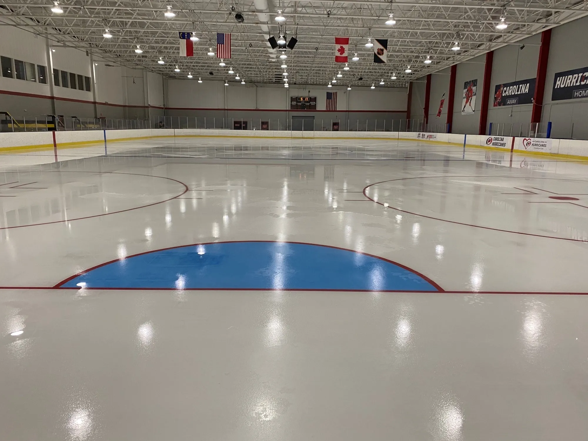 The blue goal crease with flags hanging beyond — Polar Ice Raleigh (Raleigh IcePlex)