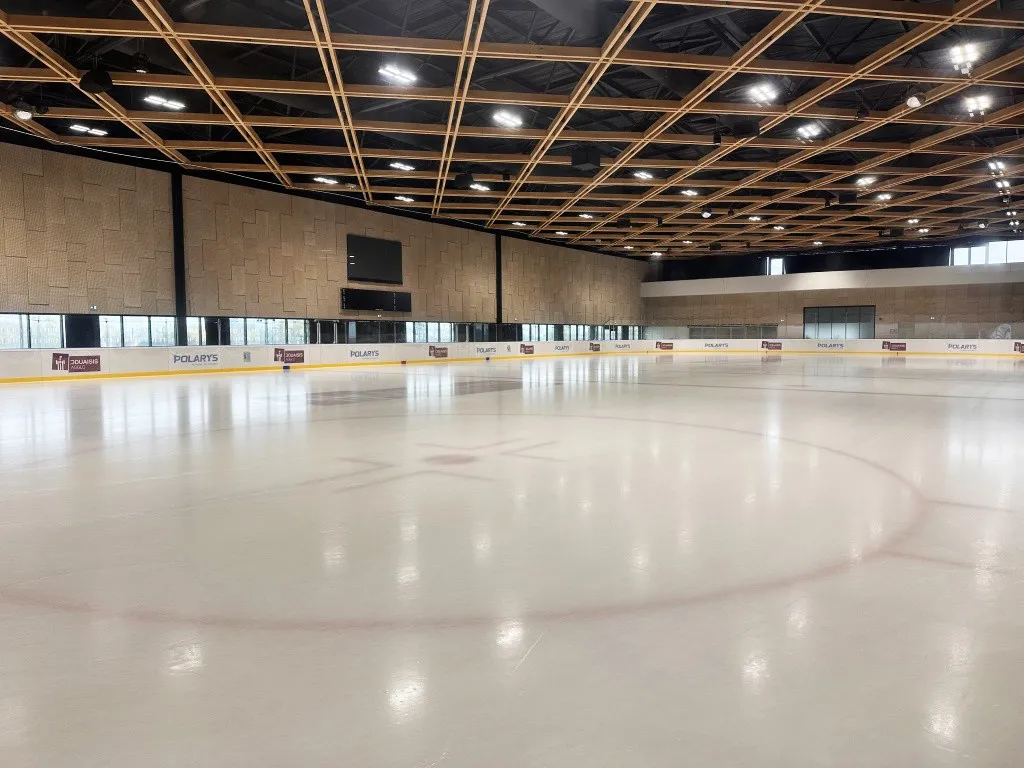 La glace vide avec son rond central et ses bandes sous une toiture en treillis de bois, avec la tribune et le mur du fond vitré derrière. — Patinoire Polarys
