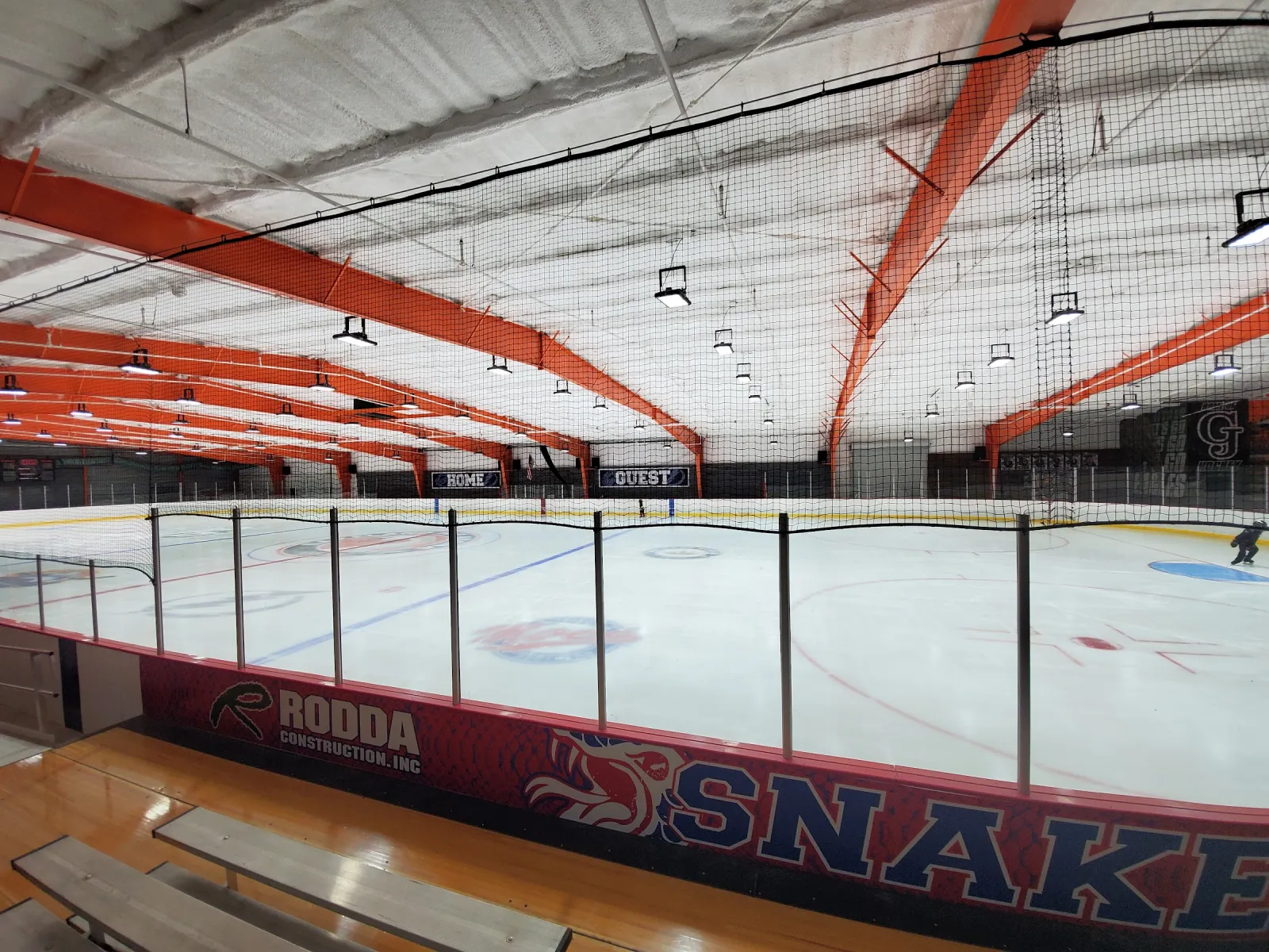 The empty rink seen from the bleachers, with red Snakes boards, the glass and orange roof trusses behind the protective netting. — Polk Athletic Complex (Lakeland)