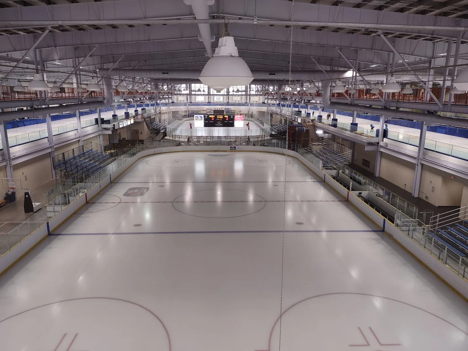 An empty NHL-size rink at the Pomeroy Sport Centre seen from the upper level, with the seating, the scoreboard at the far end and the faceoff circles in the foreground. — Pomeroy Sport Centre
