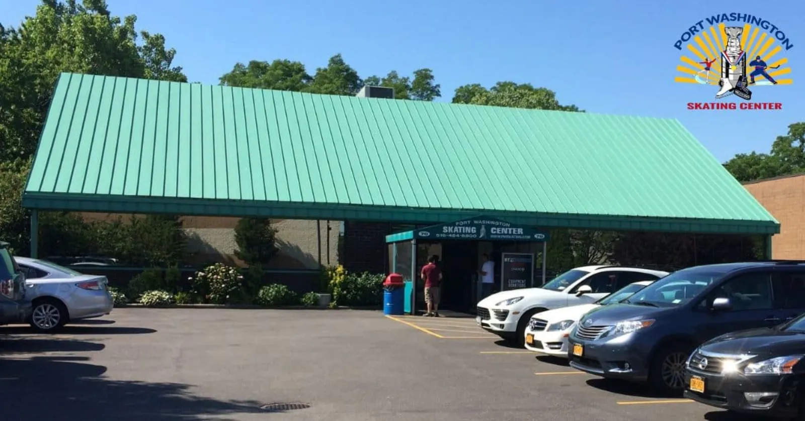 Front entrance of Port Washington Skating Center, a low building with a green standing-seam roof and 'Port Washington Skating Center' signage over the door, parking lot in front. — Port Washington Skating Center