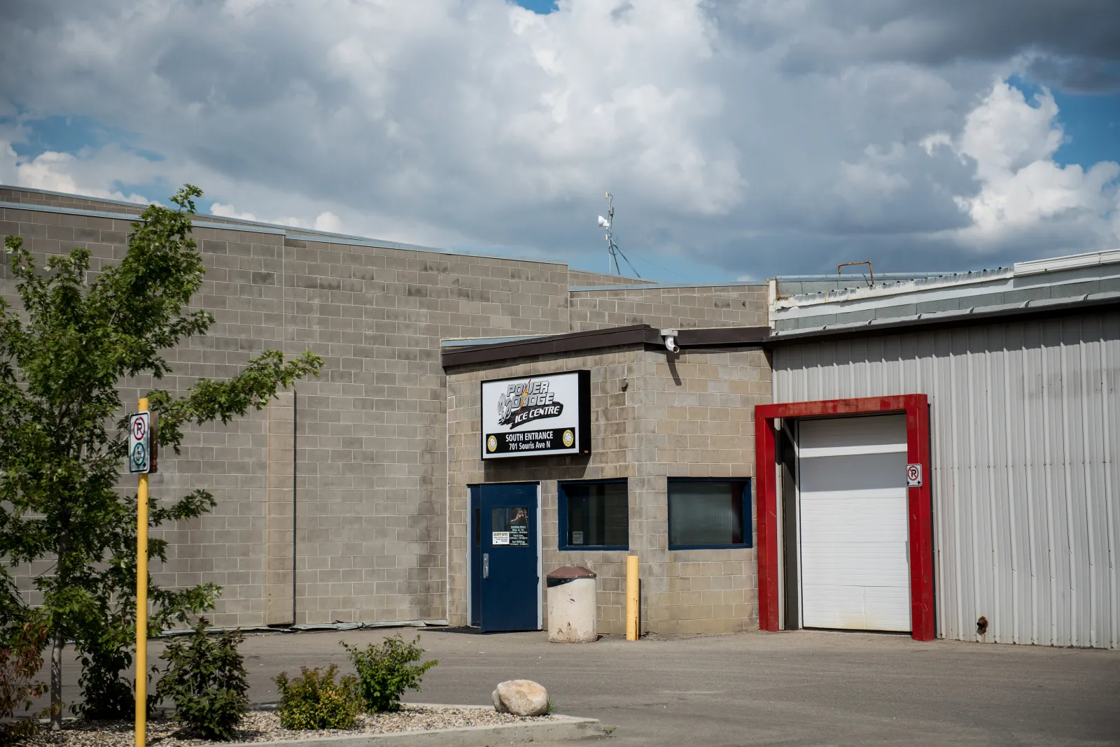 The Power Dodge Ice Centre south entrance at 701 Souris Ave N: a block building with the arena sign over a blue door, beside a garage door. — Power Dodge Arena