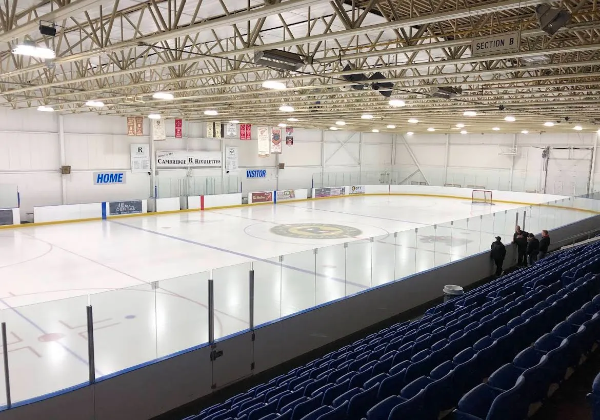 La pista vacía desde los asientos azules, con vallas blancas, un techo de armaduras de acero y el marcador en el extremo del fondo. — Preston Memorial Auditorium