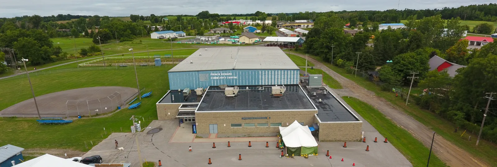 An aerial view of the Prince Edward Community Centre in Picton: the blue-clad arena with its name on the front, the parking area and the fair grounds around it. — Prince Edward Community Centre